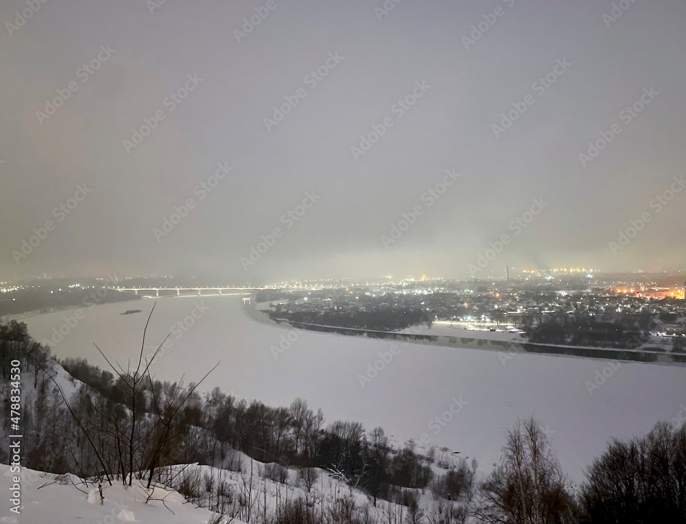 Obraz premium Far view of the city and the frozen river with bridge on a foggy winter night in Nizhny Novgorod, Russia, January 6, 2022