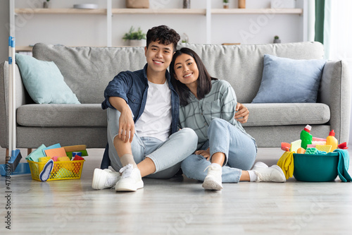 Happy asian couple sitting on floor at home, embracing