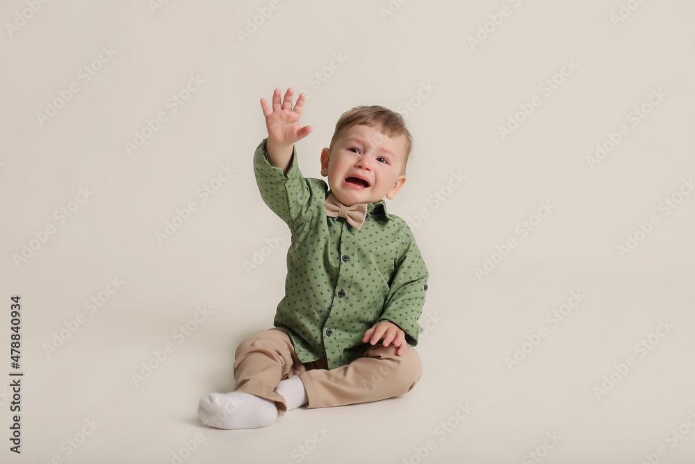 a little boy in a green shirt and bow tie beige trousers sits on a white background a little boy in a green shirt and bow tie beige trousers sits on a white background