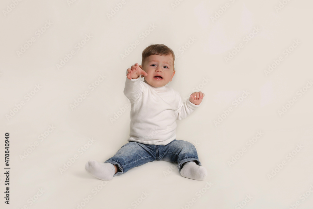 a little boy in a white jacket and jeans is sitting on a white background a little boy in a white jacket and jeans is sitting on a white background