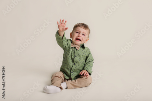 a little boy in a green shirt and bow tie beige trousers sits on a white background © Тамара Киреева