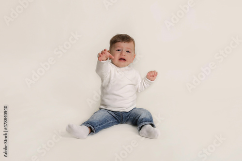 a little boy in a white jacket and jeans is sitting on a white background