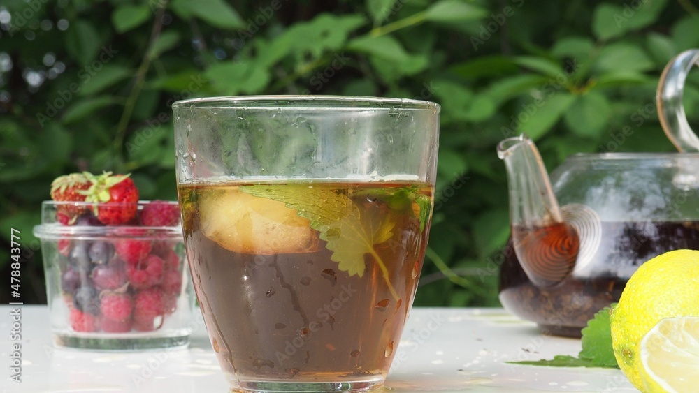 Pouring tea from a teapot into a cup on a blurred background of nature. nearby is lemon and lemongrass, wild berries. pour boiling water into a kettle to make herbal tea Pouring tea from a teapot into a cup on a blurred background of nature. nearby is lemon and lemongrass, wild berries. pour boiling water into a kettle to make herbal tea