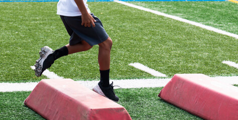 Young football player running over red barriers at pre season summer camp