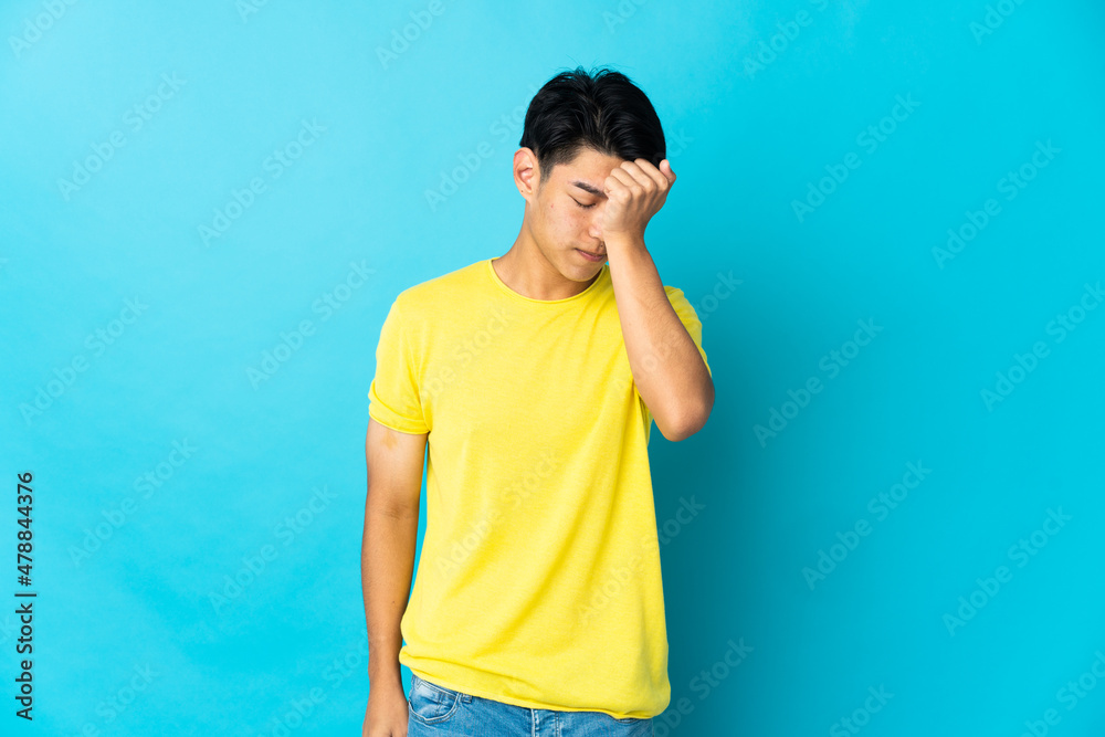 Young Chinese man isolated on blue background with headache Young Chinese man isolated on blue background with headache
