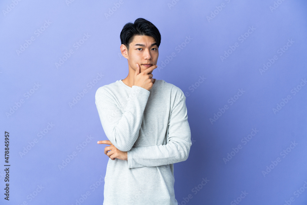 Young Chinese man isolated on purple background having doubts Young Chinese man isolated on purple background having doubts