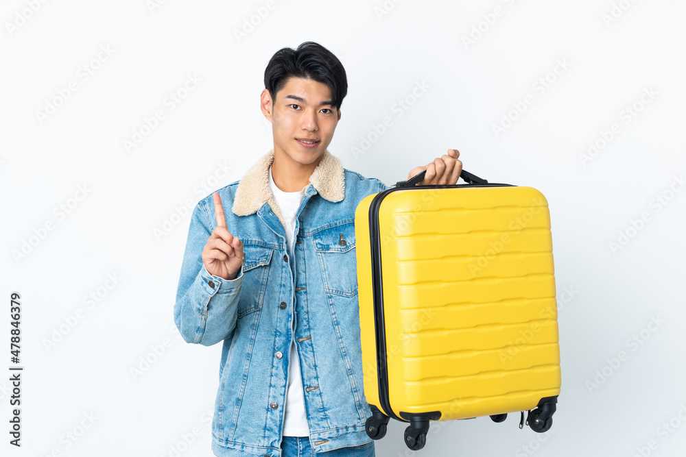Chinese man over isolated background in vacation with travel suitcase and counting one