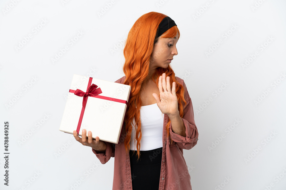 Young woman with orange hair holding a gift isolated on white background making stop gesture and disappointed Young woman with orange hair holding a gift isolated on white background making stop gesture and disappointed