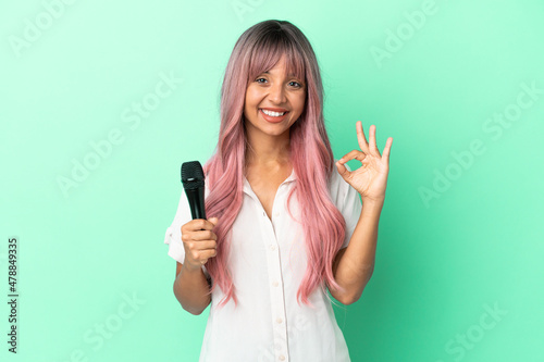 Young mixed race singer woman with pink hair isolated on green background showing ok sign with fingers