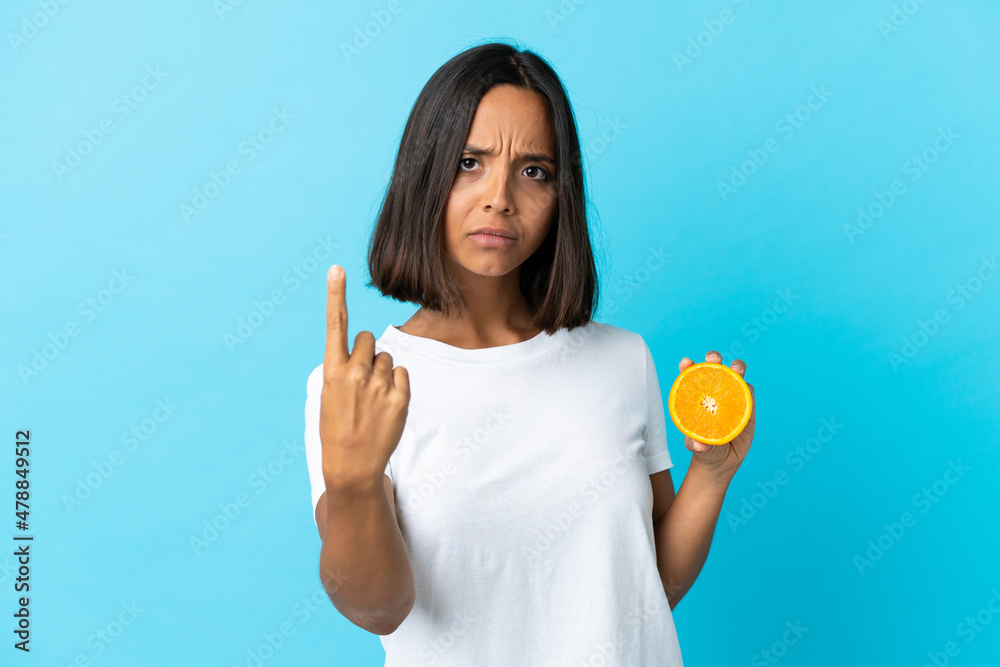 Young asian girl holding an orange isolated on blue background doing coming gesture Young asian girl holding an orange isolated on blue background doing coming gesture