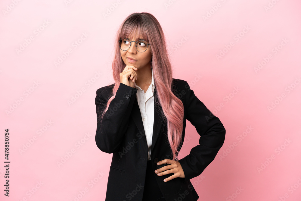 Young business mixed race woman with pink hair isolated on pink background having doubts and with confuse face expression