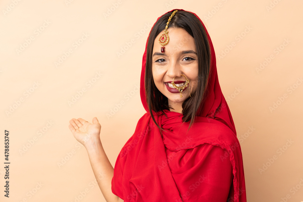 Young Indian woman isolated on beige background extending hands to the side for inviting to come Young Indian woman isolated on beige background extending hands to the side for inviting to come