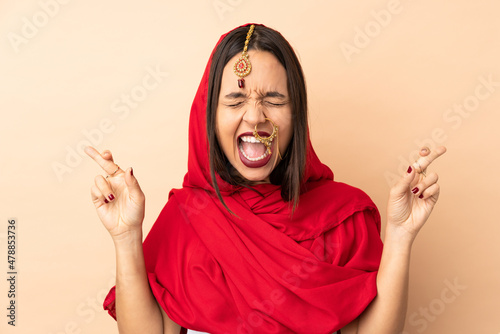 Young Indian woman isolated on beige background with fingers crossing