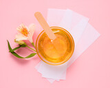 Liquid yellow sugar paste, wooden spatula, flower and depilatory strips on a pink background. Removing unwanted hair. Sugaring.Depilation. Epilation. Beauty.