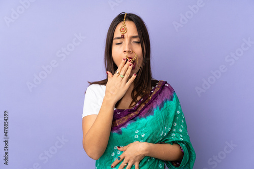 Young Indian woman isolated on purple background yawning and covering wide open mouth with hand