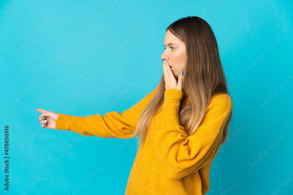 Young Lithuanian woman isolated on blue background with surprise expression while pointing side Young Lithuanian woman isolated on blue background with surprise expression while pointing side