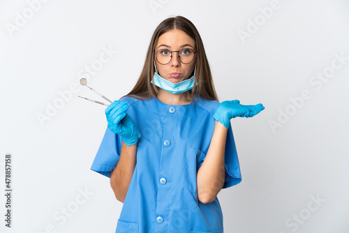 Lithuanian woman dentist holding tools over isolated background having doubts while raising hands