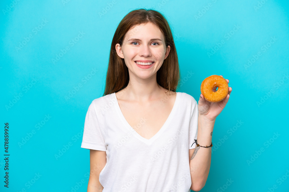 Young English woman holding a donut over isolated blue background smiling a lot Young English woman holding a donut over isolated blue background smiling a lot