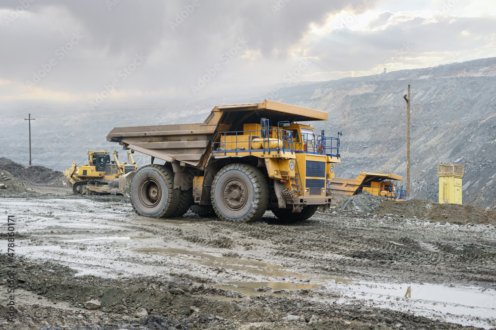 Obraz premium A large open-pit dump truck rides in an open-pit ore quarry. Part of the technological process of open-pit mining.