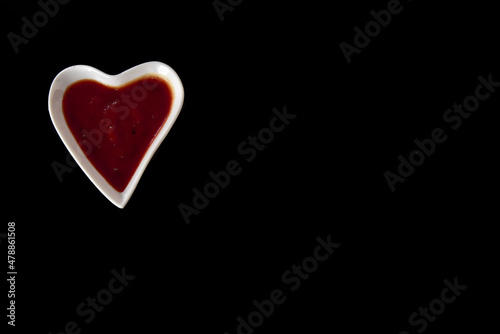 heart-shaped pot with red pepper sauce isolated on black background.