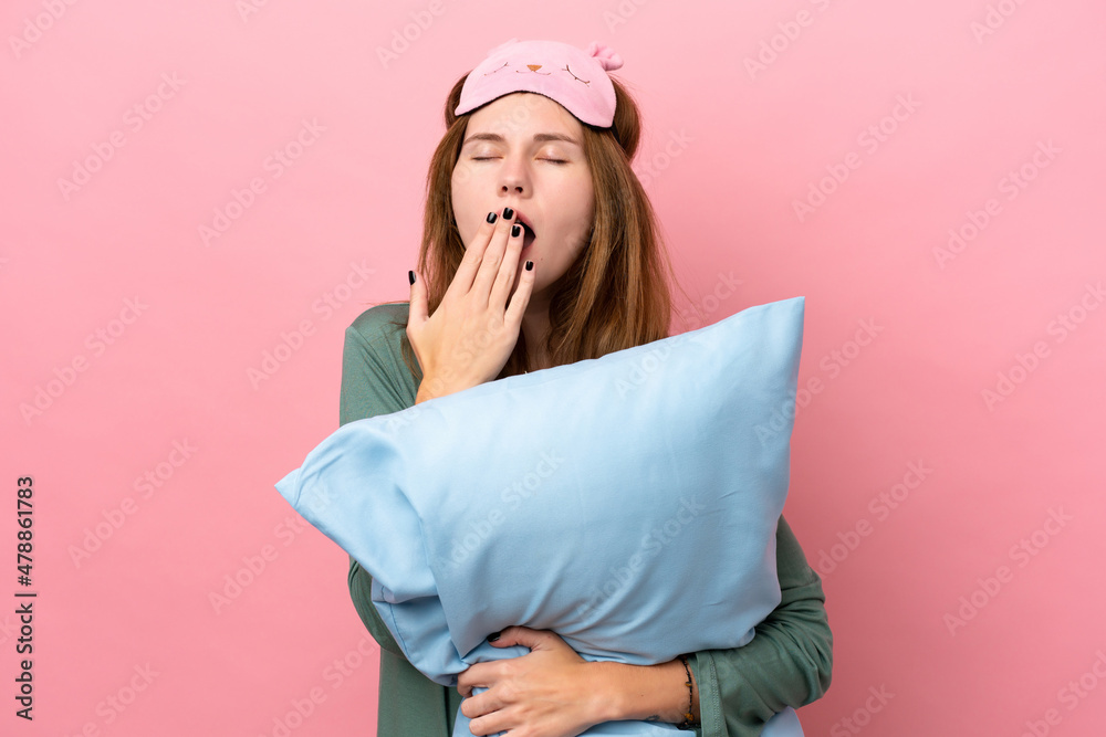 Young English woman in pajamas isolated on pink background in pajamas and holding a pillow and yawning - obrazy, fototapety, plakaty 
