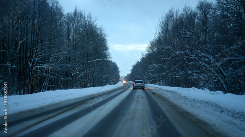 Winter. The car drives along the road with a turn through the forest. Snow-covered trees bent over the road.