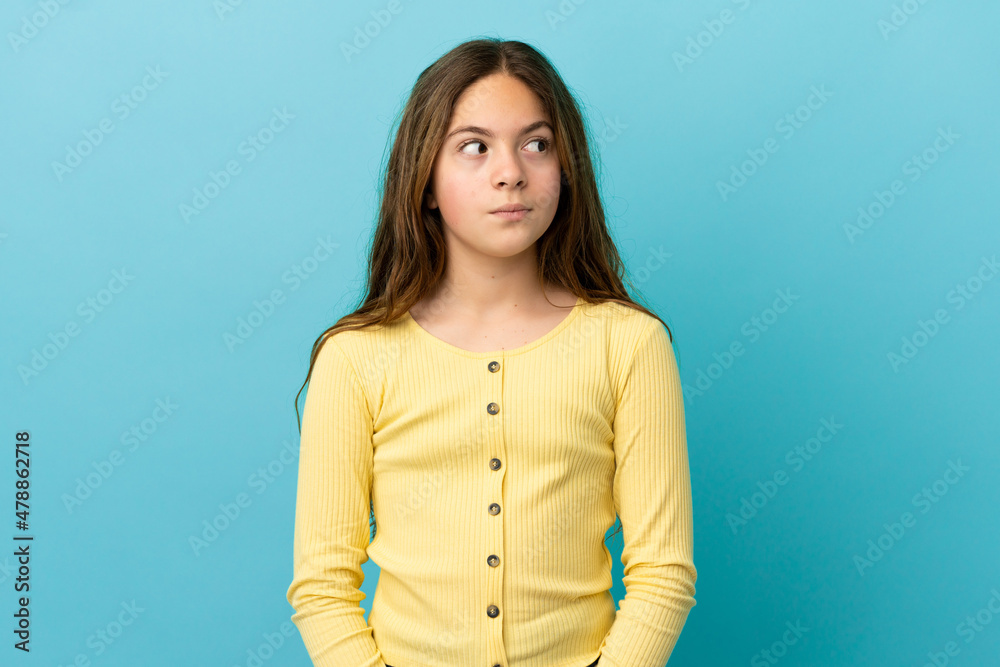 Little caucasian girl isolated on blue background making doubts gesture looking side Little caucasian girl isolated on blue background making doubts gesture looking side