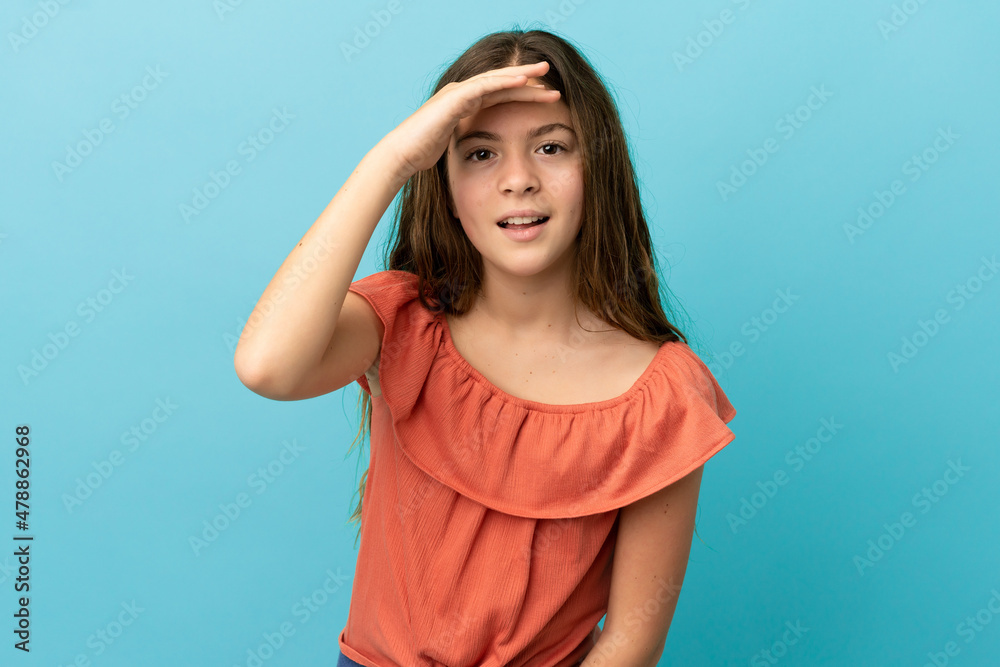 Little caucasian girl isolated on blue background looking far away with hand to look something