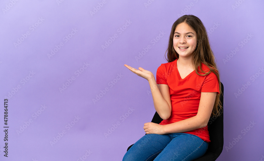 Little caucasian girl sitting on a chair isolated on purple background holding copyspace imaginary on the palm to insert an ad Little caucasian girl sitting on a chair isolated on purple background holding copyspace imaginary on the palm to insert an ad
