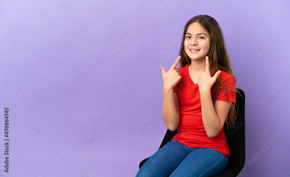 Fototapeta premium Little caucasian girl sitting on a chair isolated on purple background giving a thumbs up gesture