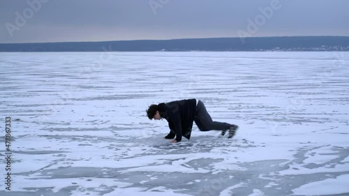 The guy walks on the frozen ice of the river and slips and falls. Winter season. Side view.