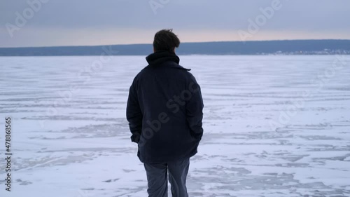 A young guy walks on a frozen lake alone. Winter season.