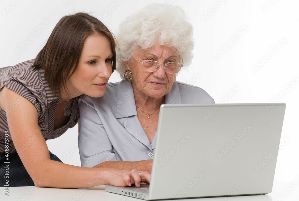 Junge Frau hilft Seniorin bei der Arbeit am Computer Junge Frau hilft Seniorin bei der Arbeit am Computer