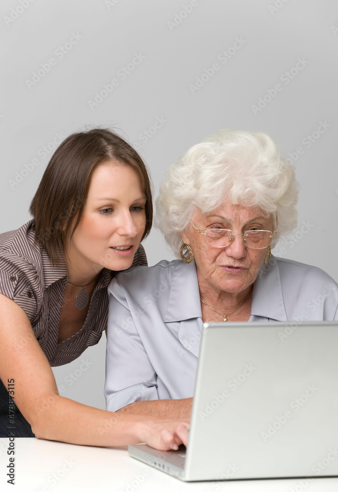 Junge Frau hilft Seniorin bei der Arbeit am Computer Junge Frau hilft Seniorin bei der Arbeit am Computer