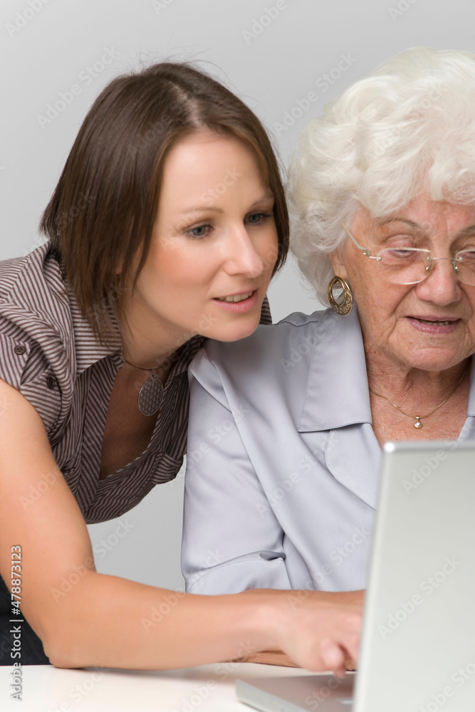 Junge Frau hilft Seniorin bei der Arbeit am Computer Junge Frau hilft Seniorin bei der Arbeit am Computer
