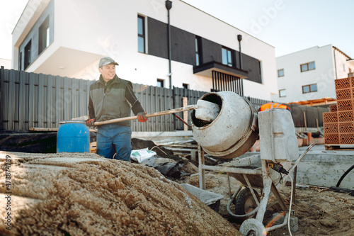 Male worker using shovel for mixing sand and cement. Construction site worker mixing cement and pouring concrete photo