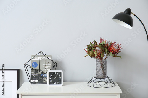 Vase with flowers  magazine and clock on shelf near light wall