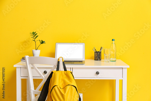 Modern workplace with laptop, glass and bottle of water near yellow wall © Pixel-Shot