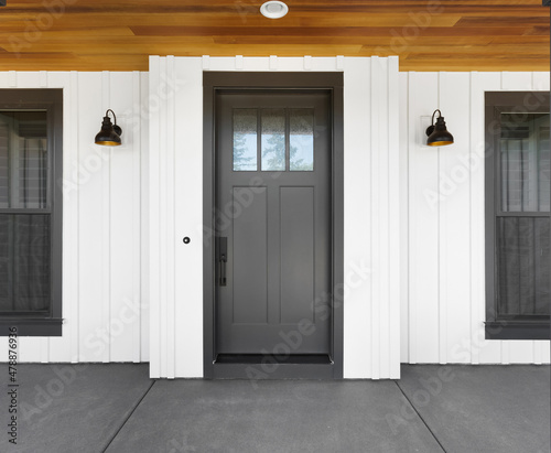 Front door to new luxury modern farmhouse style home: black front door with white vertical siding and sconce lights. Upper portion of door has glass with mullions.