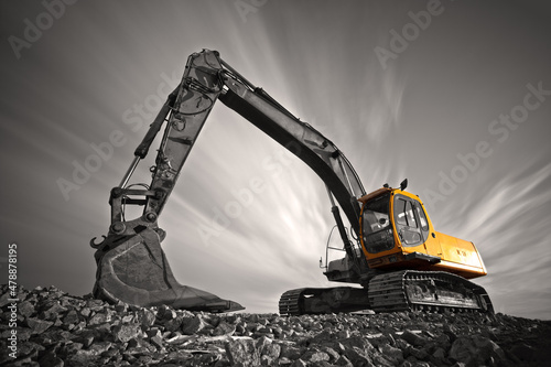 Excavator parked on stone ground against dramatic sky photo