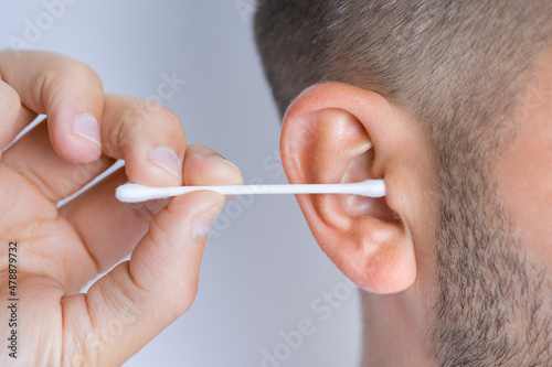 Closeup of man cleaning dirty ears with cotton swab or cotton stick. Ear cleaning and ear care photo