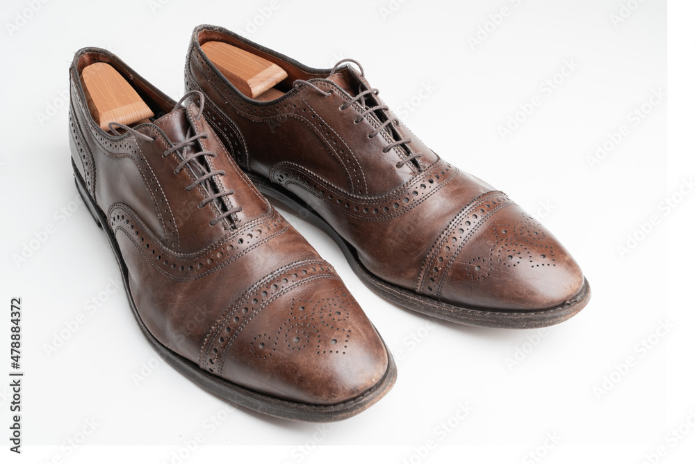 Studio shot of old, weary and little scratched cap toe lace op oxford shoes in burnished brown color, on white background. Shoe trees inserted. Old shoes before cleaning and polishing.