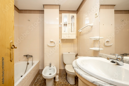 Conventional toilet with white bidet and fixtures and cream-toned walls