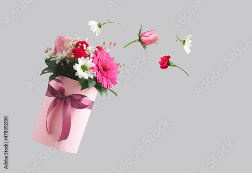 Pink gift box with various flowers on grey background. Flying flowers from the box. Valentines day aesthetic nature concept. 8 March card idea.