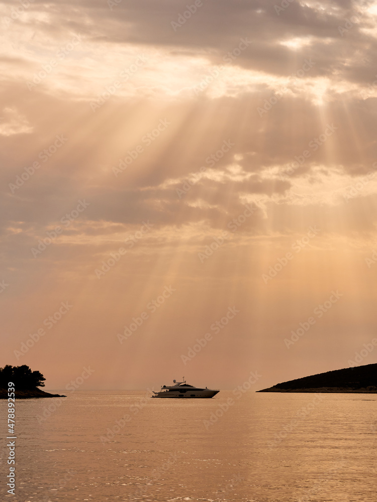 Silhouette of the yacht and islands in the rays of sunlight penetrating through thick clouds
