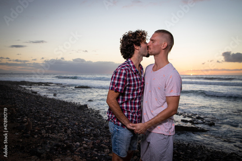 Gay couple kissing at the beach during sunset in summer. Same sex couple on vacation, partners in love. Romantic and passionate moment - Valentine's Day gay couple concept
