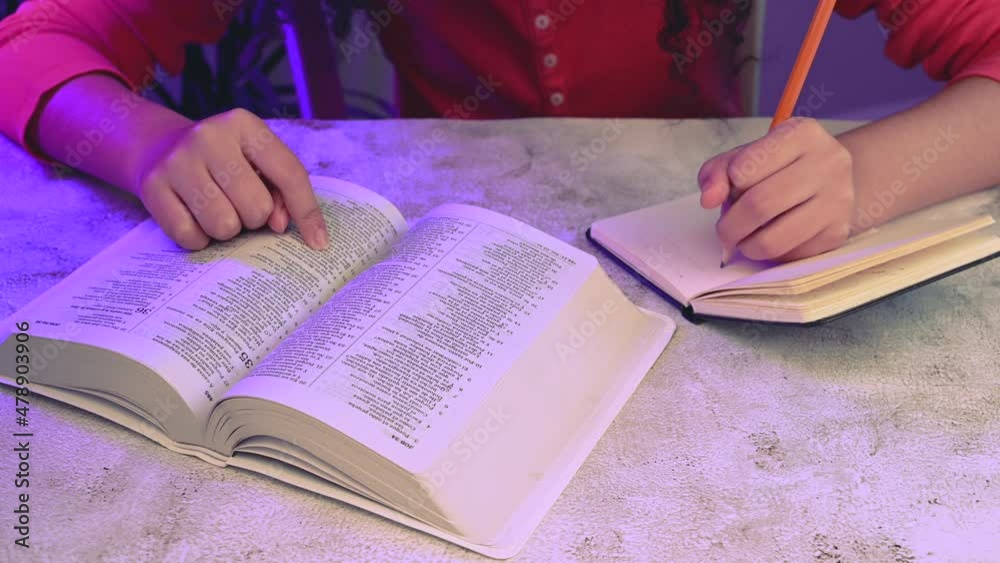 Close up of mixed race teenager doing notes on notebook and reading the christian bible.