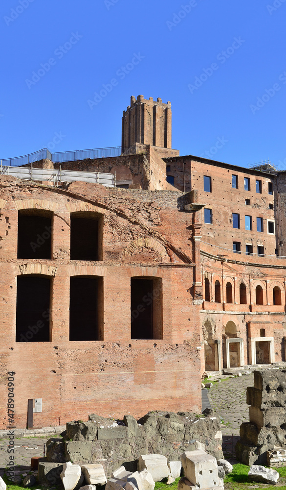 Blue sky, green grass, tower of Milizie and ancient ruins of the Trajan market in Rome, Italy. Brick walls under the blue sky