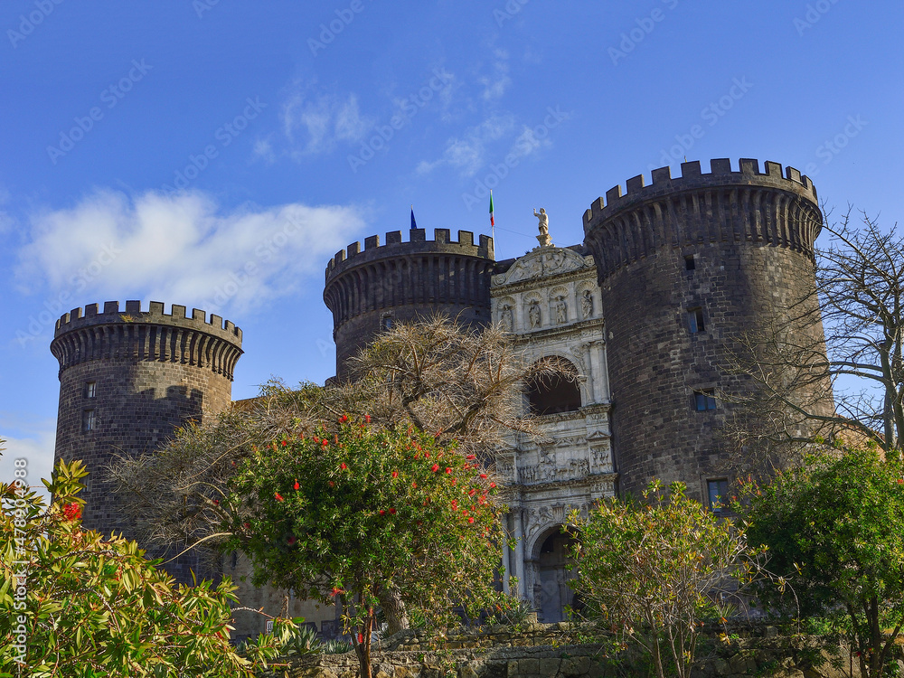 Blue sky, green trees and Castel Nuovo (New Castle), also called Maschio Angioino (Angevin Keep), ia medieval castle in central Naples, Campania, Italy.