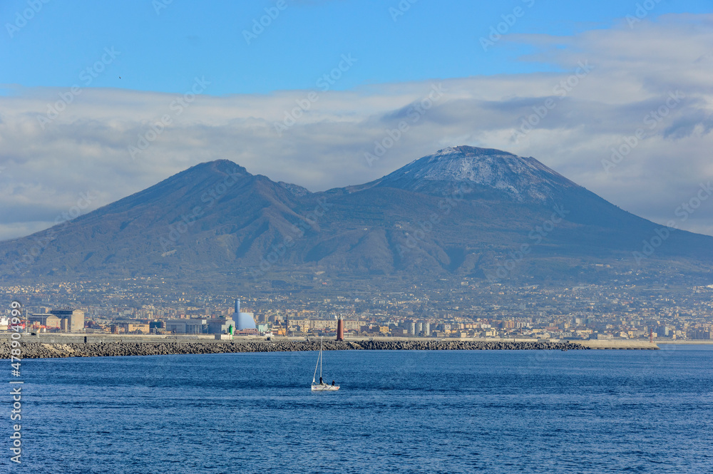 Gulf of Naples, mount Vesuvius and a small sailboat in the blue sea under the blue sky with clouds